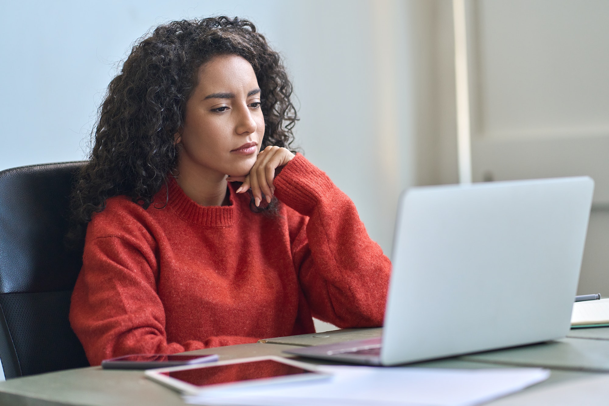 Young latin business woman working on laptop thinking analyzing online data.